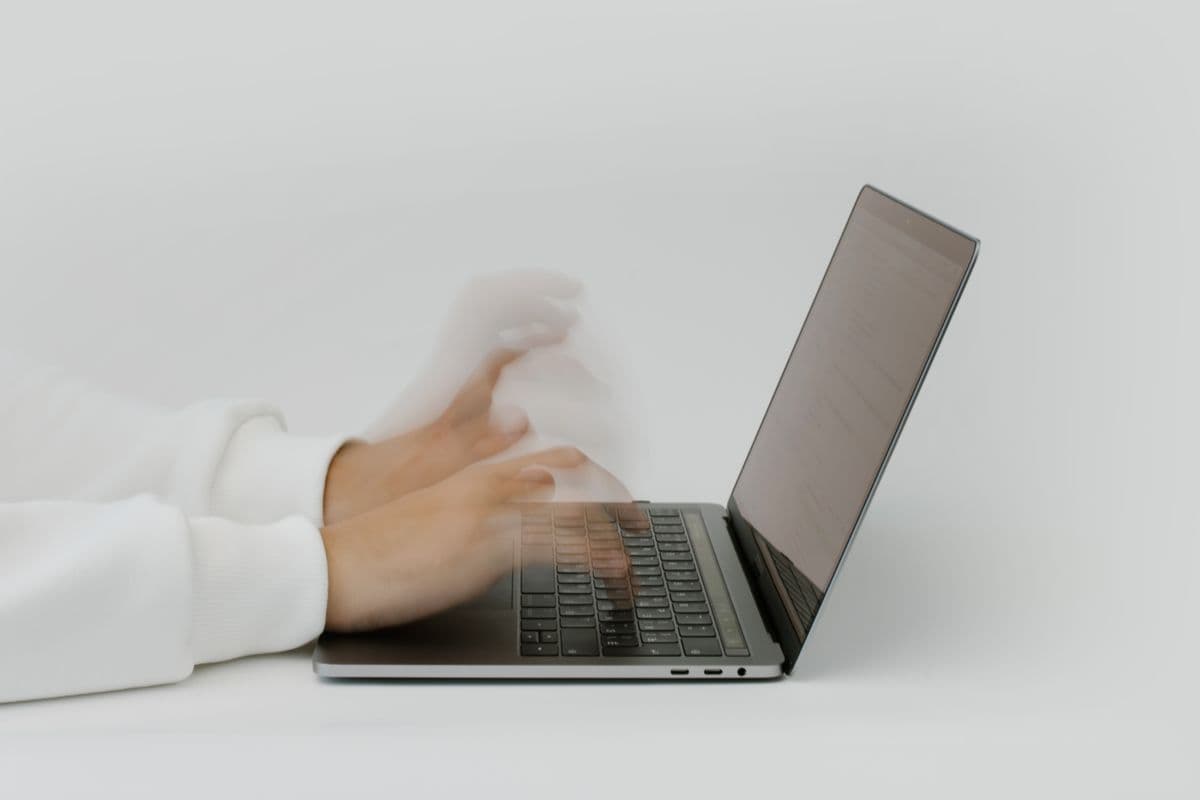 Motion-blurred hands typing rapidly on a laptop against a plain background