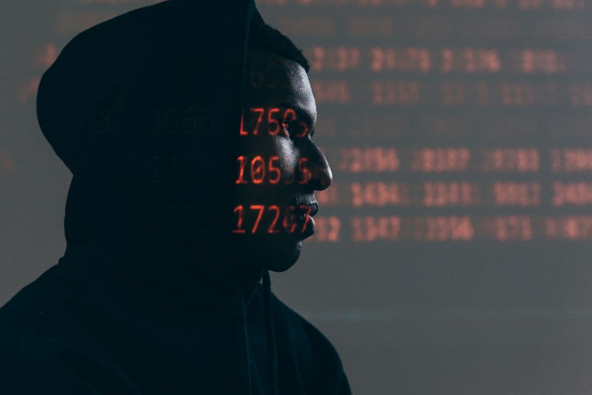 A person in a hooded sweatshirt in profile, with rows of red data projected across their face