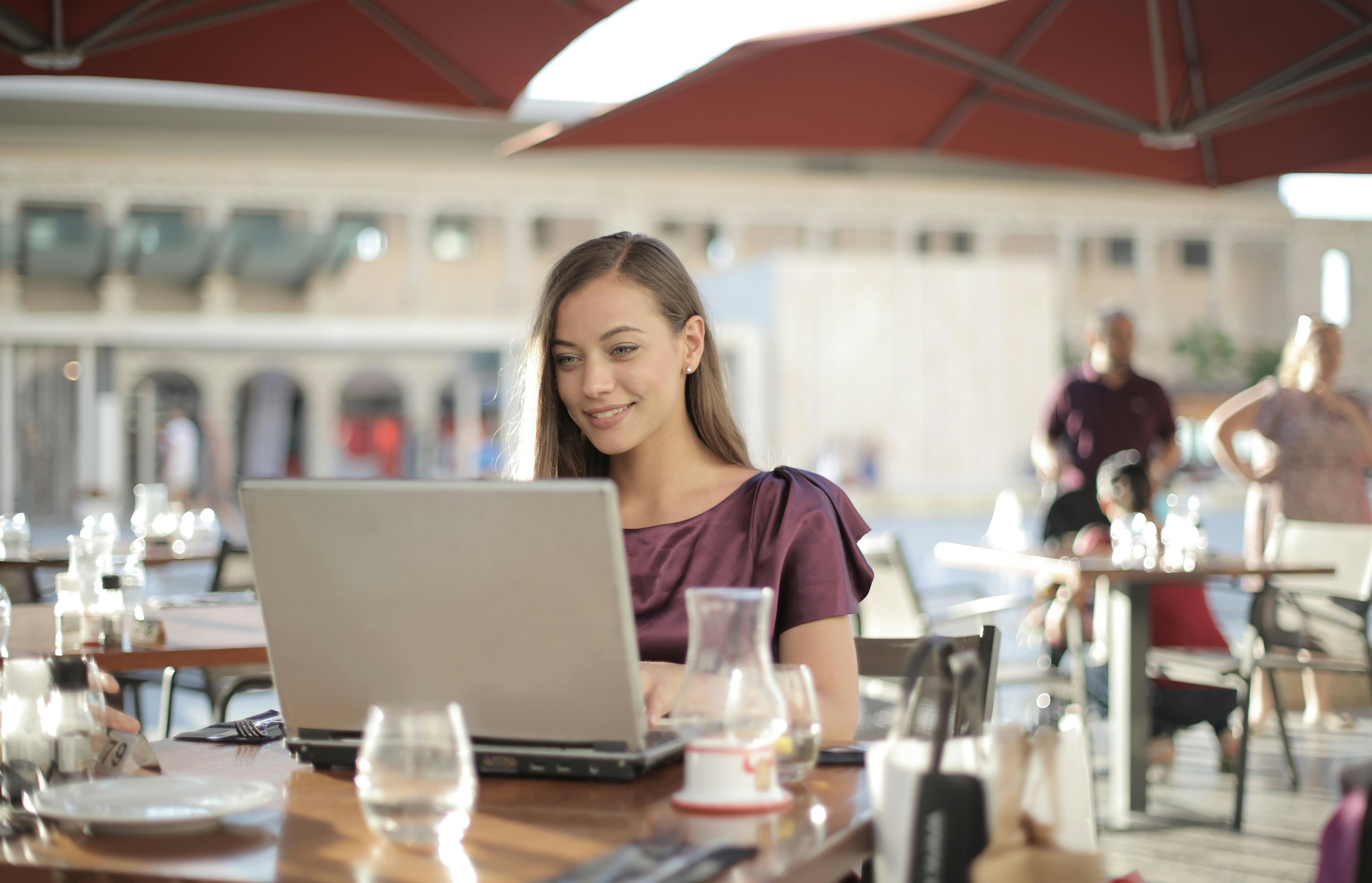 A remote worker smiling at a laptop on an outdoor cafe terrace
