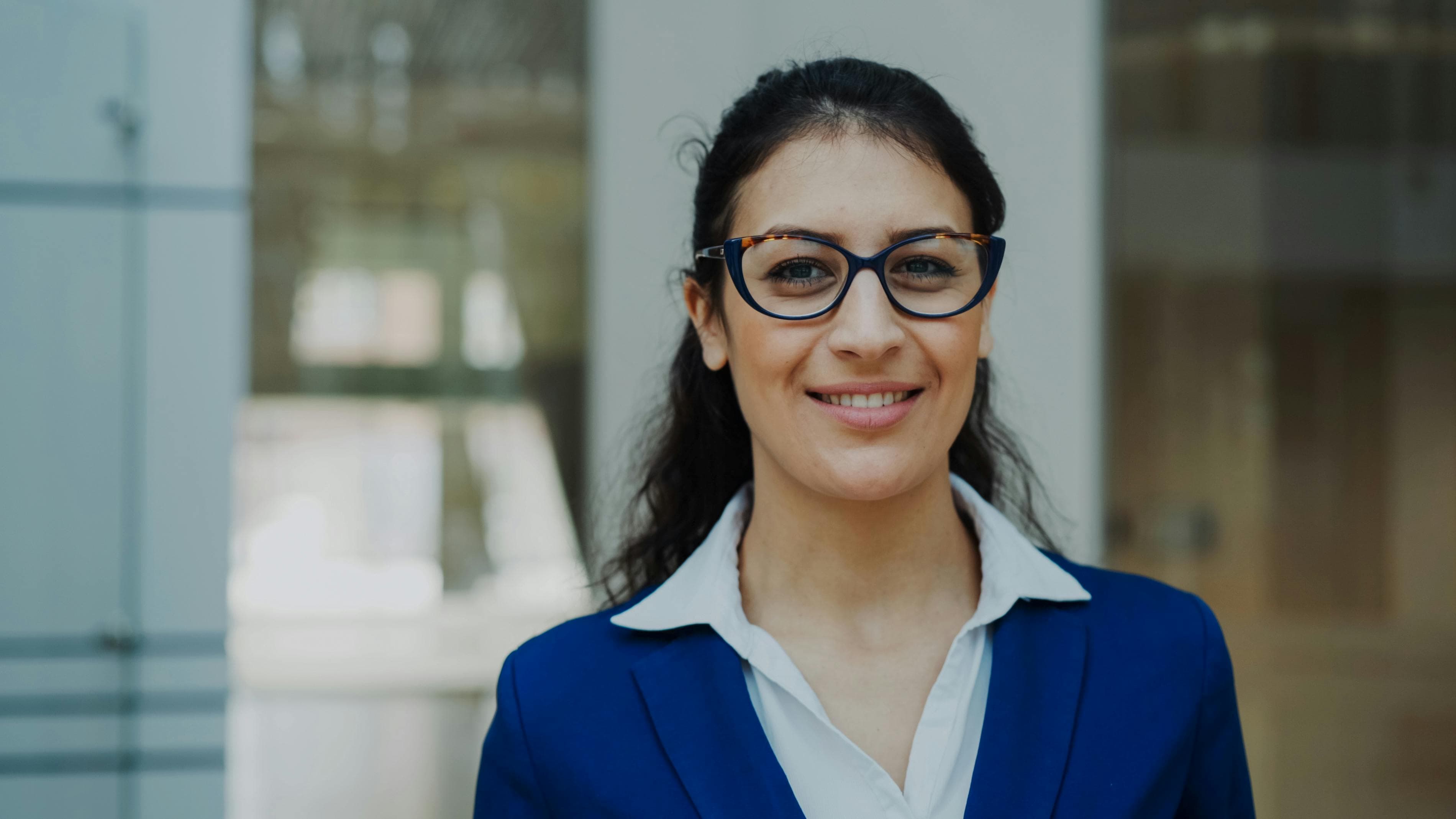 A confident professional in glasses and a blue blazer looking directly at the camera