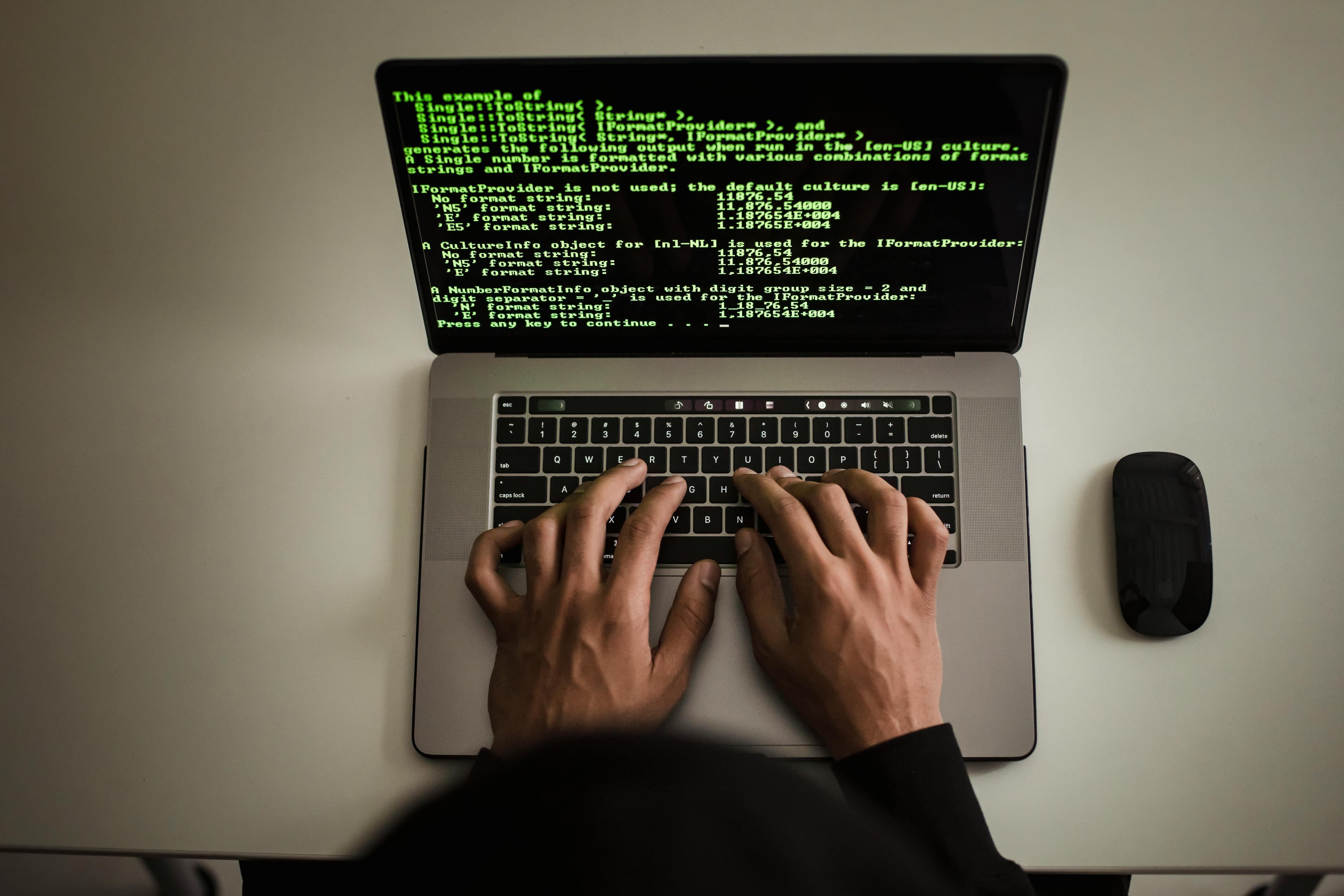 Hands typing on a laptop displaying green terminal code in a dark setting